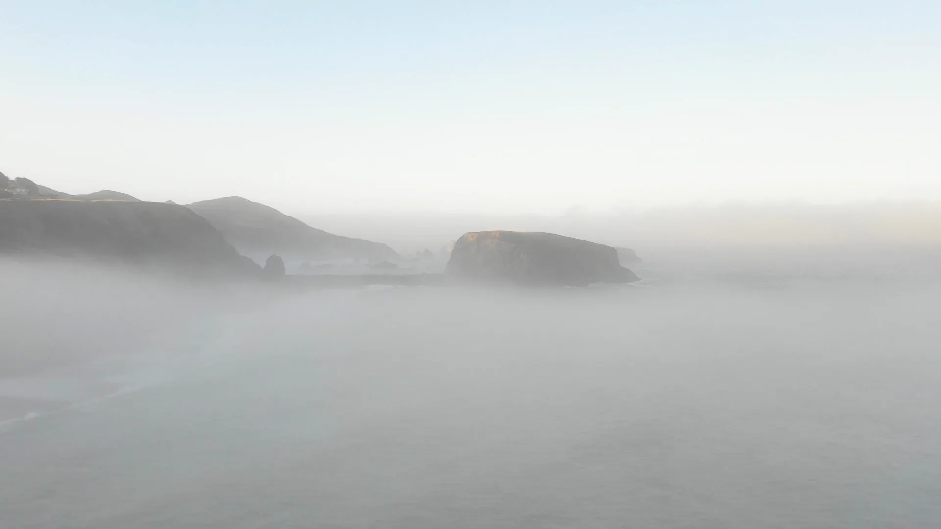 Fog drifting across a rocky coastline as waves roll toward shore